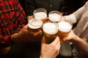Close-up of five men toasting with beer while sitting in beer pu